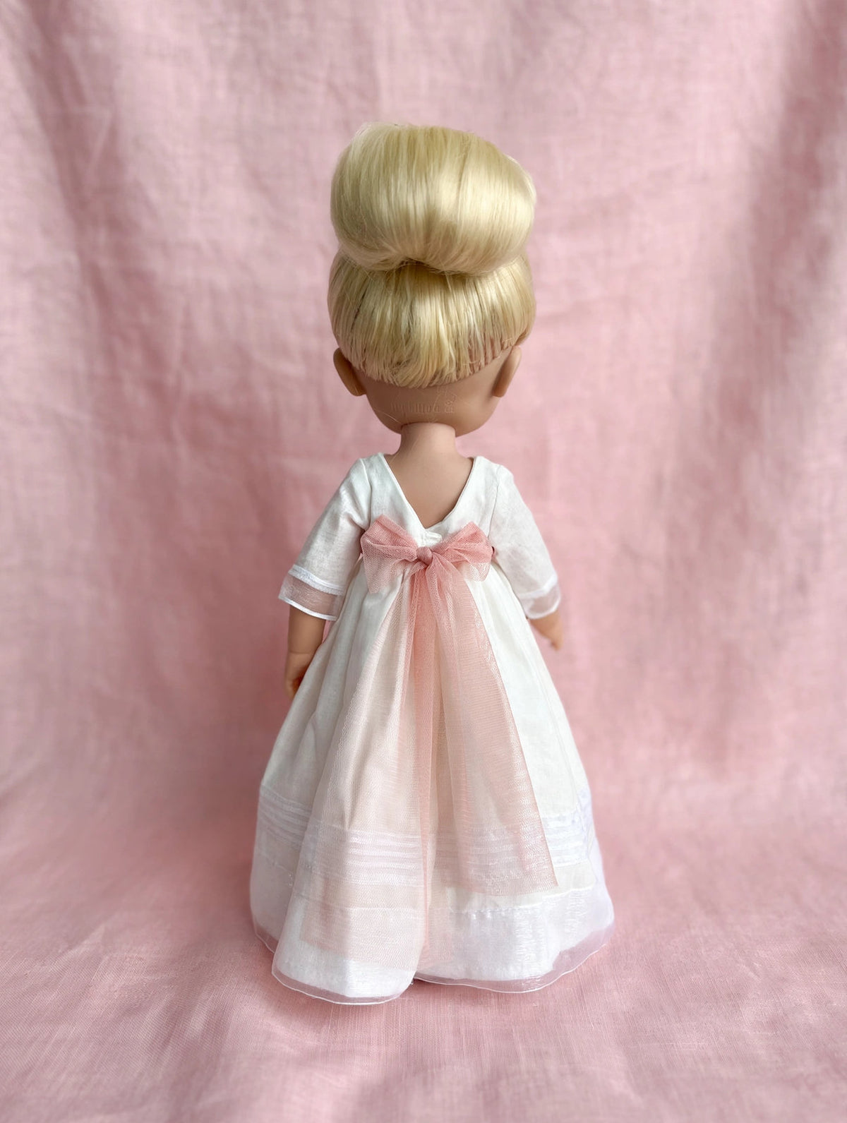 Vista de espaladas de la muñeca de comunión personalizada con vestido Marieta liso y con organza de rayas. Puedes elegir la muñeca que quieras (rubia, morena, pelirroja, ojos azules, verdes o azules), el fajín, los zapatos y todos los detalles como los de la niña. Sólo en My little twin.