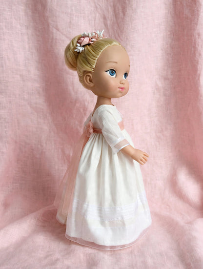 Vista lateral de la muñeca de comunión personalizada con vestido Marieta liso y con organza de rayas. Puedes elegir la muñeca que quieras (rubia, morena, pelirroja, ojos azules, verdes o azules), el fajín, los zapatos y todos los detalles como los de la niña. Sólo en My little twin.